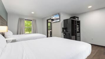 A hotel room with two beds, a TV, a wardrobe, and a window with curtains.