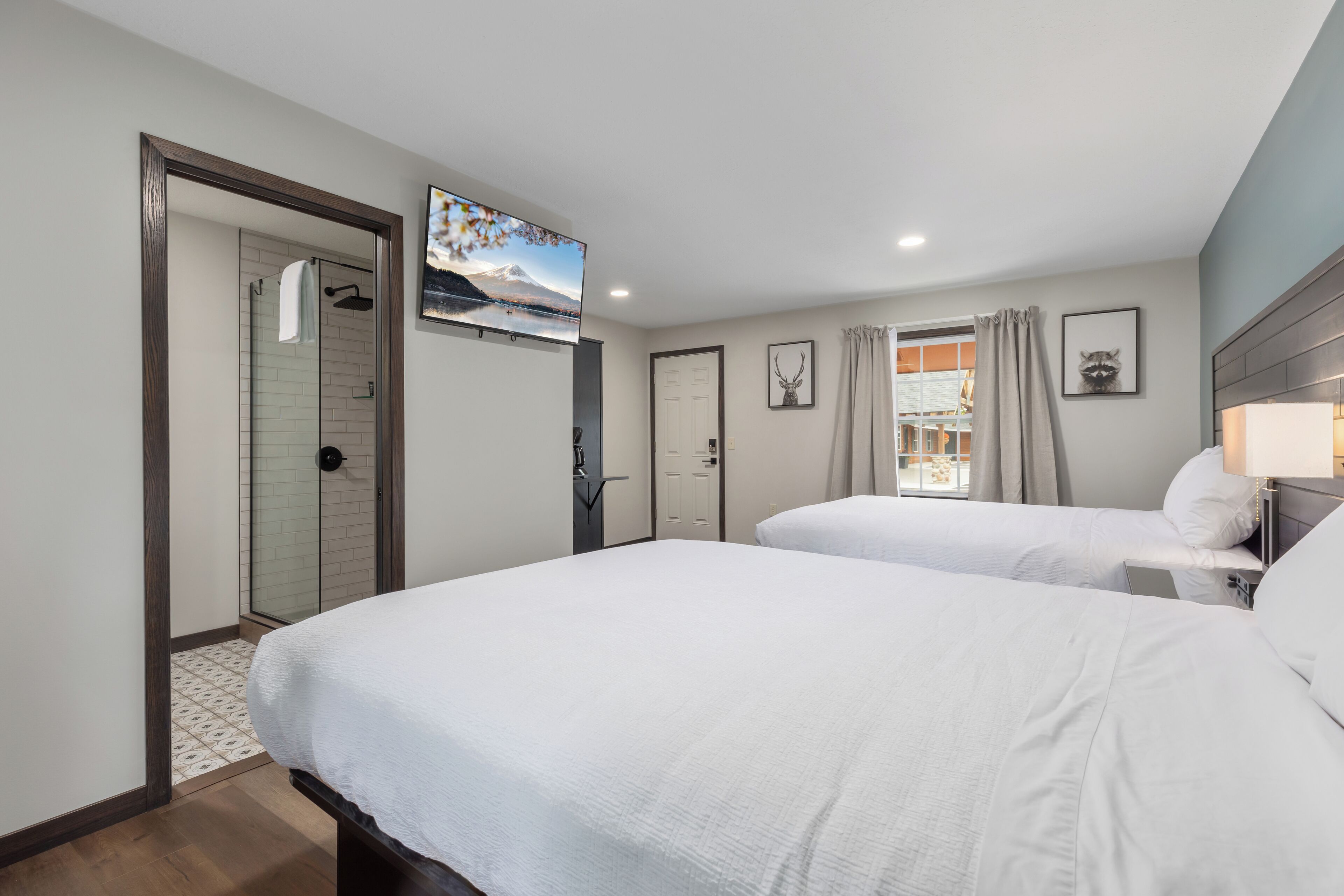 A hotel room with two beds, a TV, a shower, and a window with curtains.