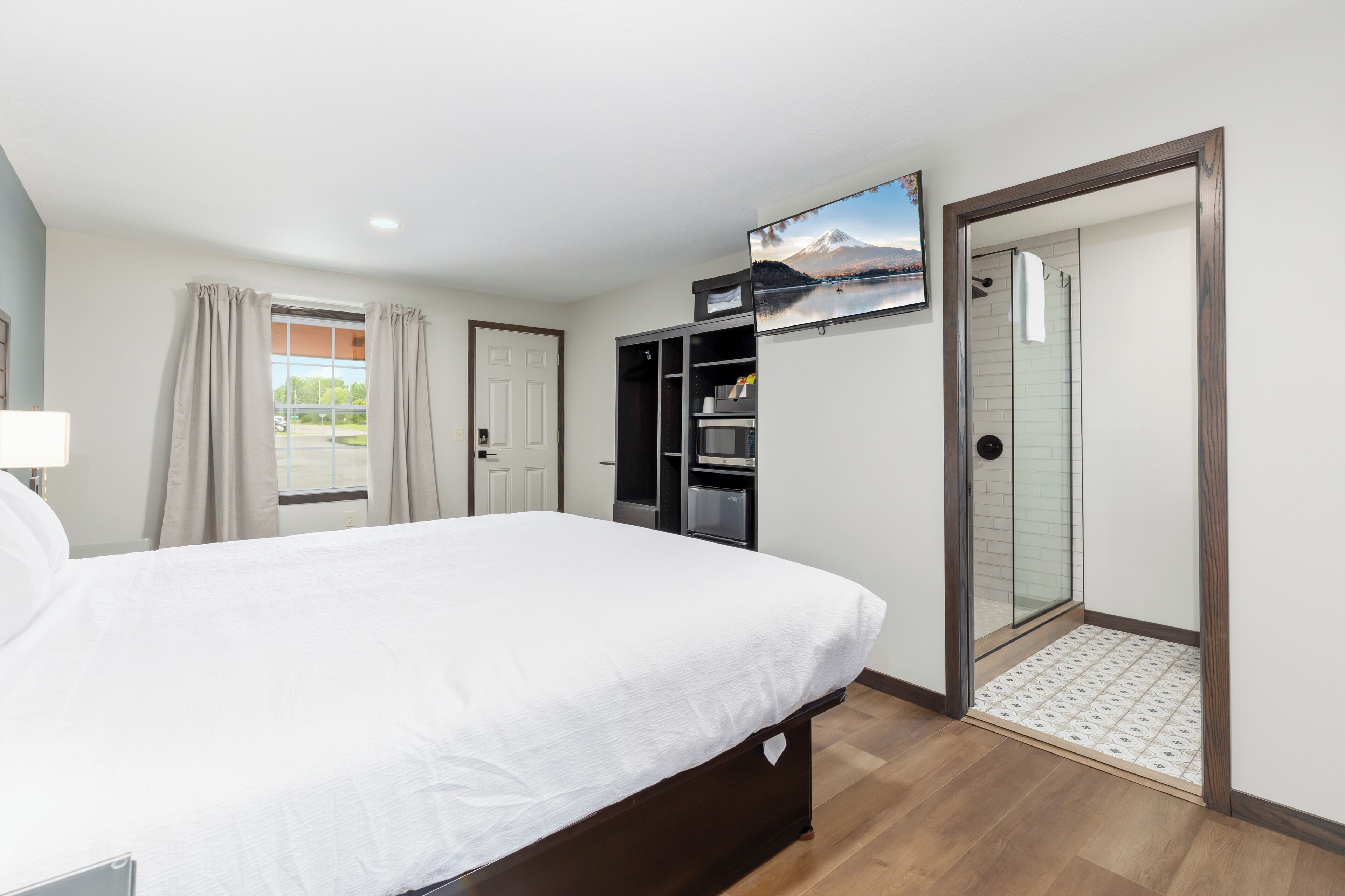 A hotel room with a bed, a wardrobe, a shower area, and a mounted TV.