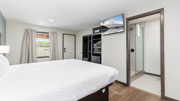 Ein Hotelzimmer mit Bett, Kleiderschrank, Duschbereich und einem an der Wand befestigten Fernseher.