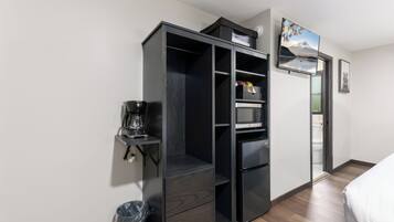 A compact room with a kitchenette, a bed, a trash bin, and a door leading to a bathroom.