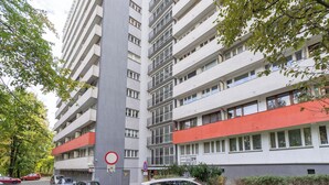 A multi-story residential building with balconies, a parking area, and a red and white facade. - Park Śląski Comfy Apartment (Katowice)