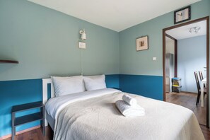 Un dormitorio con cama, mesita de noche, lámpara de pared y puerta que da a otra habitación.