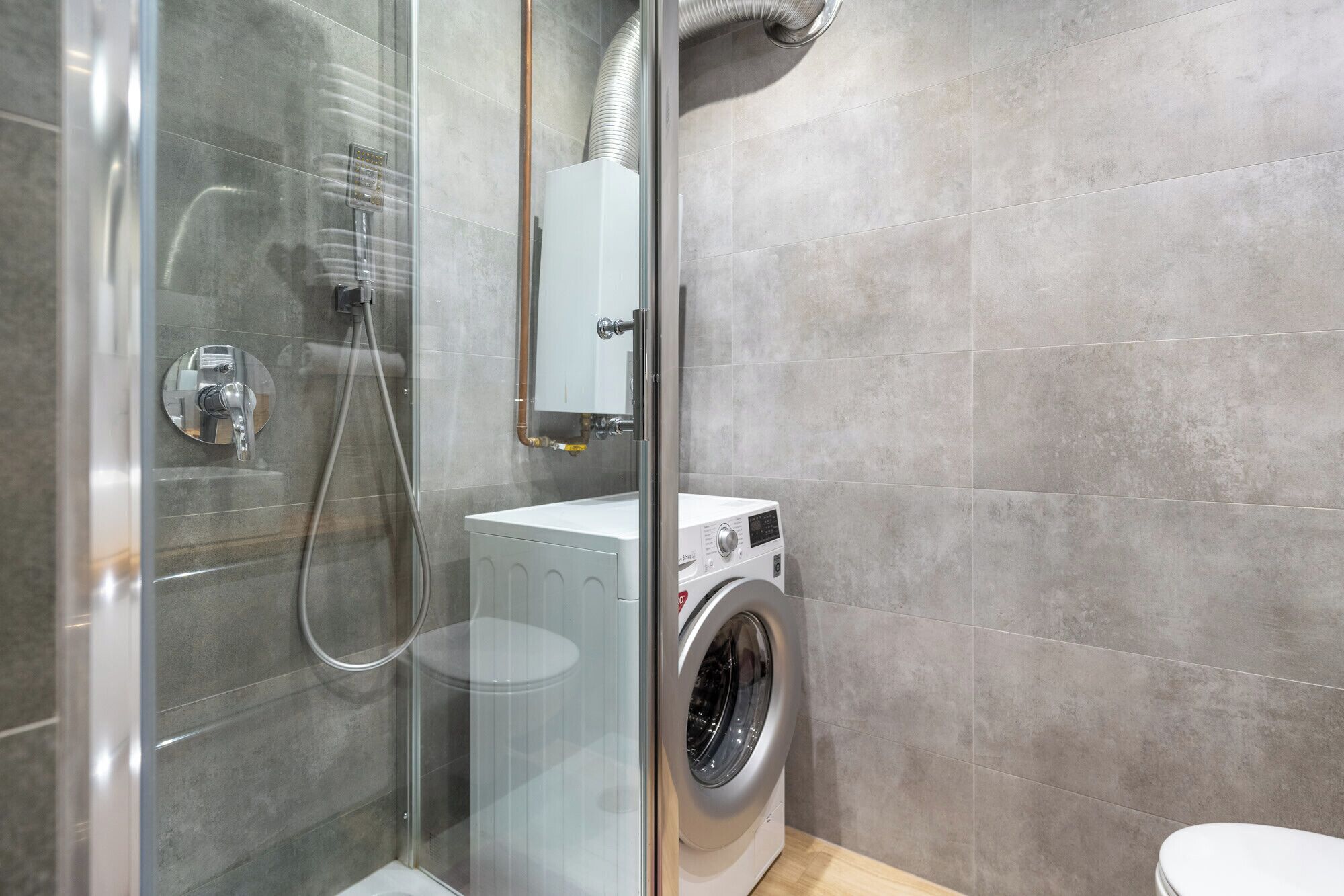 A modern bathroom with a glass-enclosed shower, a built-in washing machine, and a toilet.