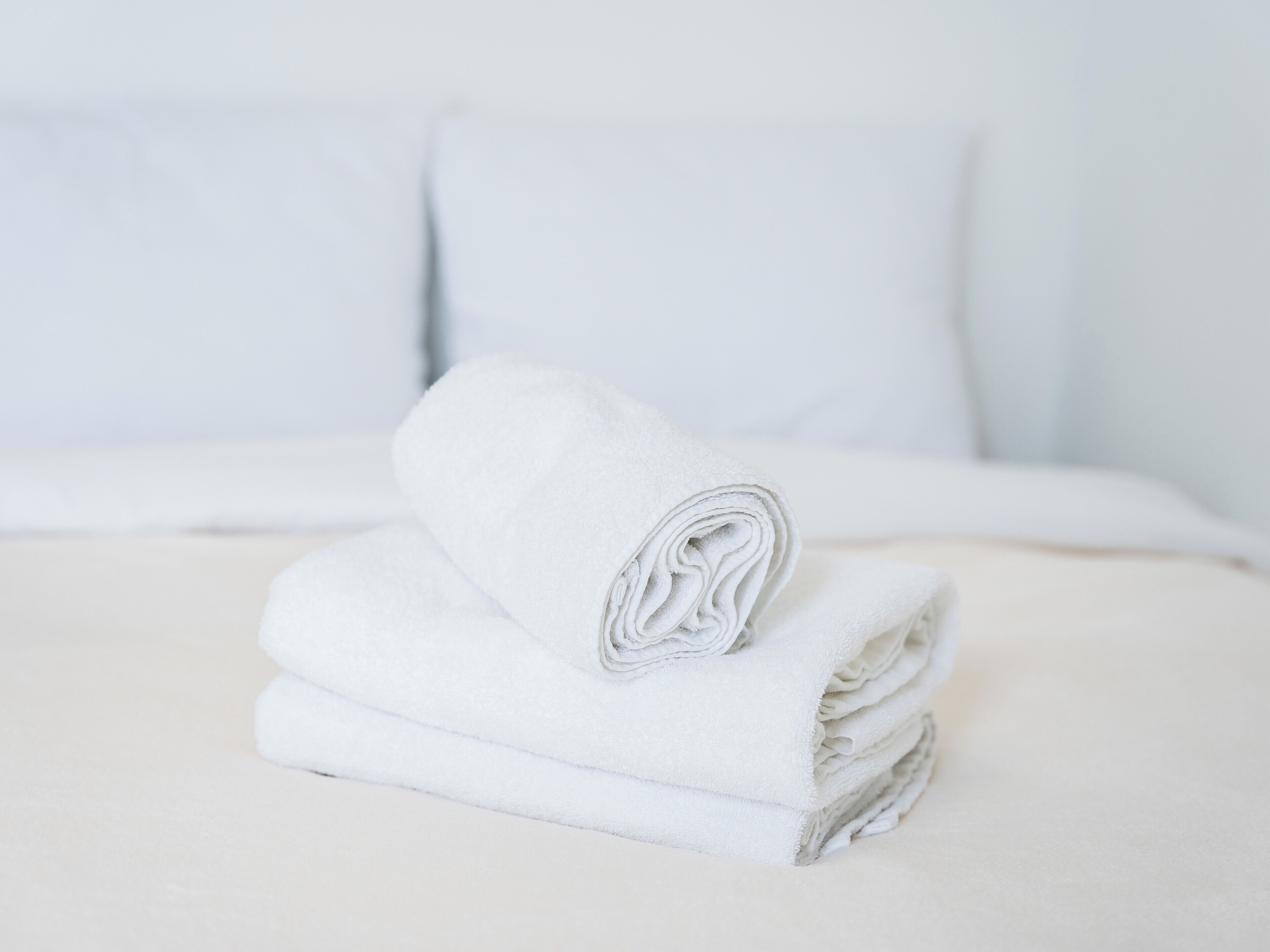Una toalla blanca doblada cuidadosamente sobre una cama con ropa de cama y almohadas blancas.