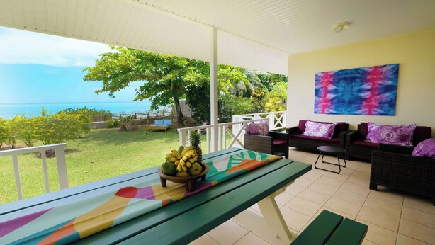 Un'area relax all'aperto con vista sul mare, un tavolo con una ciotola di frutta e un quadro astratto dai colori vivaci appeso alla parete.