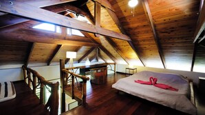 Una stanza con soffitto alto e travi in legno, un letto con un asciugamano a forma di cuore, una lampada e una scala.