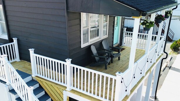 Une maison à deux étages avec une terrasse en bois, des rampes blanches et un porche couvert comprenant des chaises et une table.