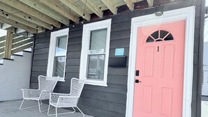 Un bâtiment avec une porte rose, deux fenêtres et un porche avec des chaises blanches.