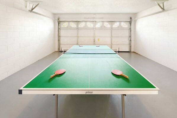 A ping pong table with two paddles in a garage with white brick walls and a garage door.