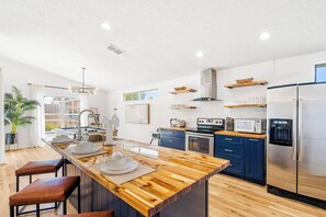 Une cuisine moderne dotée d’un îlot central, d’appareils électroménagers en acier inoxydable et offrant une vue sur l’extérieur.