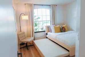 A bedroom with a bed, a chair, a window, and a lamp.