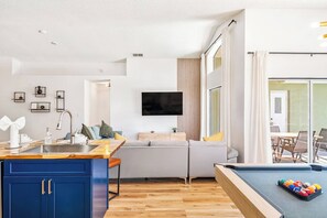 A modern living room with a sofa, a television, and a pool table.