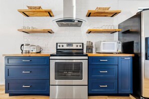 A kitchen with a stainless steel oven, a microwave, and wooden shelves above the counter.