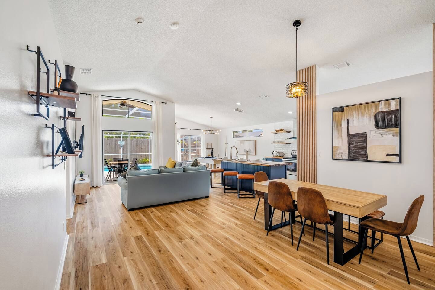 A modern kitchen with a central island, a dining area with wooden chairs, and a large window providing natural light.