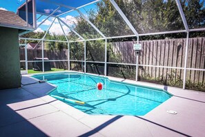A backyard with a swimming pool, a covered patio area, and a wooden fence.
