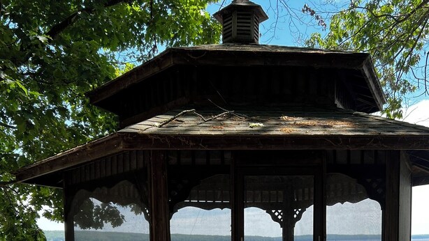 Ein hölzernes Gartenhaus mit Gitterveranda, mit Blick auf ein Gewässer.