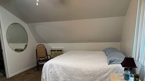 Ein Schlafzimmer mit einem Bett, einem Deckenventilator, einem Sessel, einem Nachttisch mit Lampe und einem Fenster.