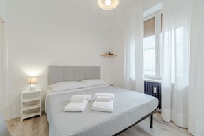 Un dormitorio minimalista con cama, mesita de noche y ventana con cortinas.