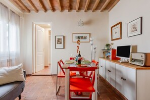 A dining area with a table set for two, red chairs, a white cabinet with a television, and framed pictures on the wall. - GuestHost - The Sun of Florence Home (Firenze)