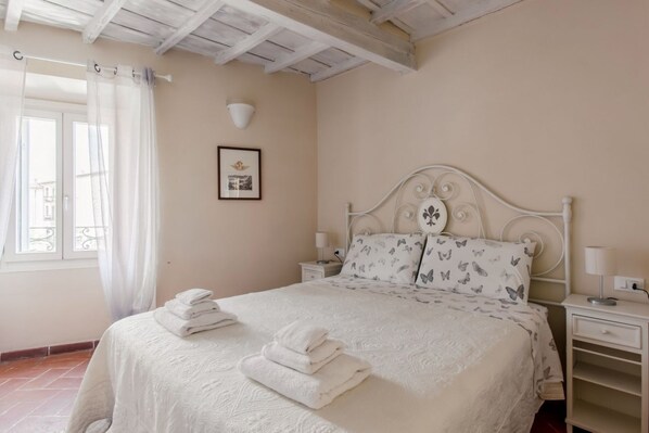 A bedroom with a bed, white curtains, a framed picture, a bedside table with a lamp, and a nightstand with a lamp. - GuestHost - The Sun of Florence Home (Firenze)