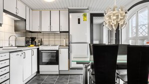 A modern kitchen with white cabinets, a built-in oven, a refrigerator, and a dining area with a glass table and black chairs. - Awesome home in øster assels with WiFi (Øster Assels)
