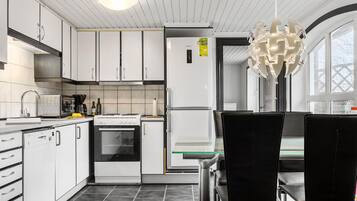 A modern kitchen with white cabinets, a built-in oven, a refrigerator, and a dining area with a glass table and black chairs.