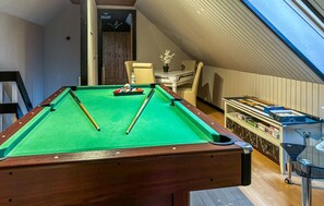 A pool table in a room with a sloped ceiling, a wooden door, and a small table with a vase of flowers.