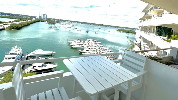 A balcony with white furniture overlooking a marina with numerous boats. - Cozy Studio with the Best Miami Skyline Views and free parking (North Bay Village)