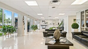 A spacious lobby with a modern design, featuring a black leather sofa, a coffee table with magazines, and potted plants. - Cozy Studio with the Best Miami Skyline Views and free parking (North Bay Village)