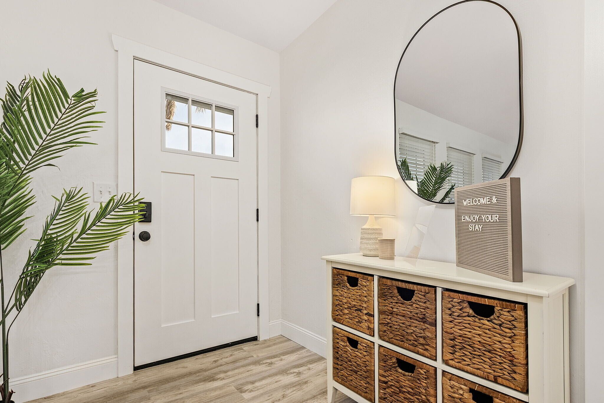 A hallway with a white door, a mirror, a lamp, and a welcome sign.