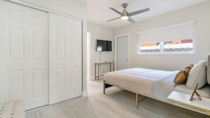 A bedroom with a bed, a TV, a ceiling fan, and a window with a view. - TWO Casitas | Victoria Park | 30+ Night Stays Only (Fort Lauderdale)