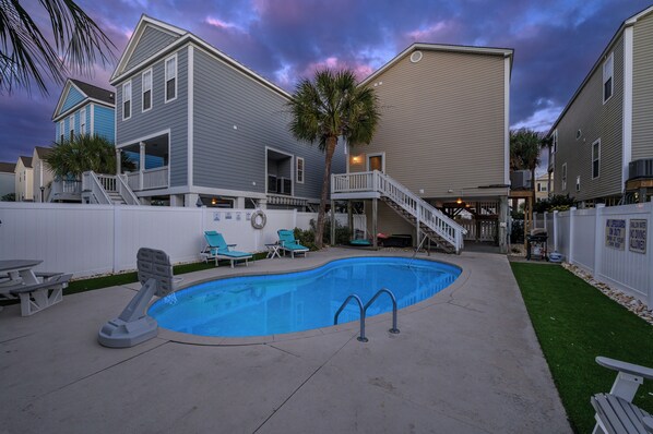 A residential backyard with a swimming pool, a slide, and a staircase leading to a deck.