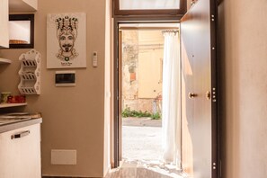Une vue intérieure d’une chambre d’hôtel, avec une porte donnant sur un espace extérieur, une œuvre d’art accrochée au mur et une petite étagère sur laquelle sont posés divers objets.