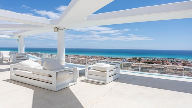 Una terraza en la azotea con mobiliario blanco y vista al océano.