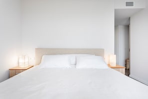 Una cama bien hecha con sábanas blancas, un cabecero de madera y dos lámparas de noche en mesitas.