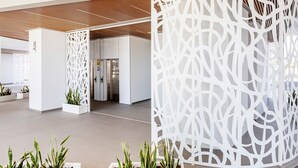 Un moderno vestíbulo de hotel con paneles decorativos blancos, techo de madera y plantas en macetas.