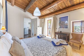 Ein Schlafzimmer mit einem großen Bett, Holzboden, Schreibtisch, Stuhl und einem Fenster mit Vorhängen.