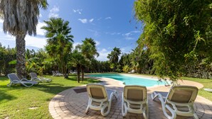A poolside area with lounge chairs, a brick patio, and lush greenery.