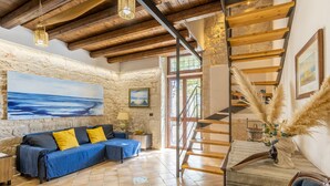 A room with a stone wall, a blue sofa, a wooden staircase, and a painting.