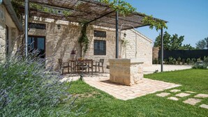 Ein Gebäude aus Stein mit einer Pergola, Sitzgelegenheiten im Freien und einem Steingarten.