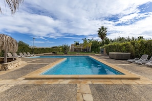 Une piscine divisée en deux zones distinctes, entourée de chaises longues et bordée d’une terrasse en pierre.