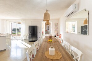 Un grand espace dédié à la salle à manger, avec une table en bois, des chaises blanches, un réfrigérateur noir et un luminaire suspendu.