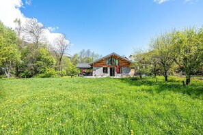A wooden cabin with a stone foundation, surrounded by a lush green field and trees. - Chalet 'De L'alpette' with Mountain View, Private Terrace and Wi-Fi (Valloire)