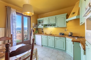 A kitchen with green cabinets, a wooden dining table, and a window with a view. - Villa 'La Petite Colline À Céret' – Mountain View, Terrace, Garden & Wi-Fi (Céret)