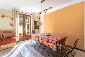 A dining area with a striped tablecloth, a sofa, and a view through a glass door. - Villa 'La Petite Colline À Céret' – Mountain View, Terrace, Garden & Wi-Fi (Céret)