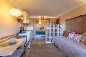 A compact room with a bed, a dining table, a kitchenette, and a view of the outside. - Villa 'La Petite Colline À Céret' – Mountain View, Terrace, Garden & Wi-Fi (Céret)