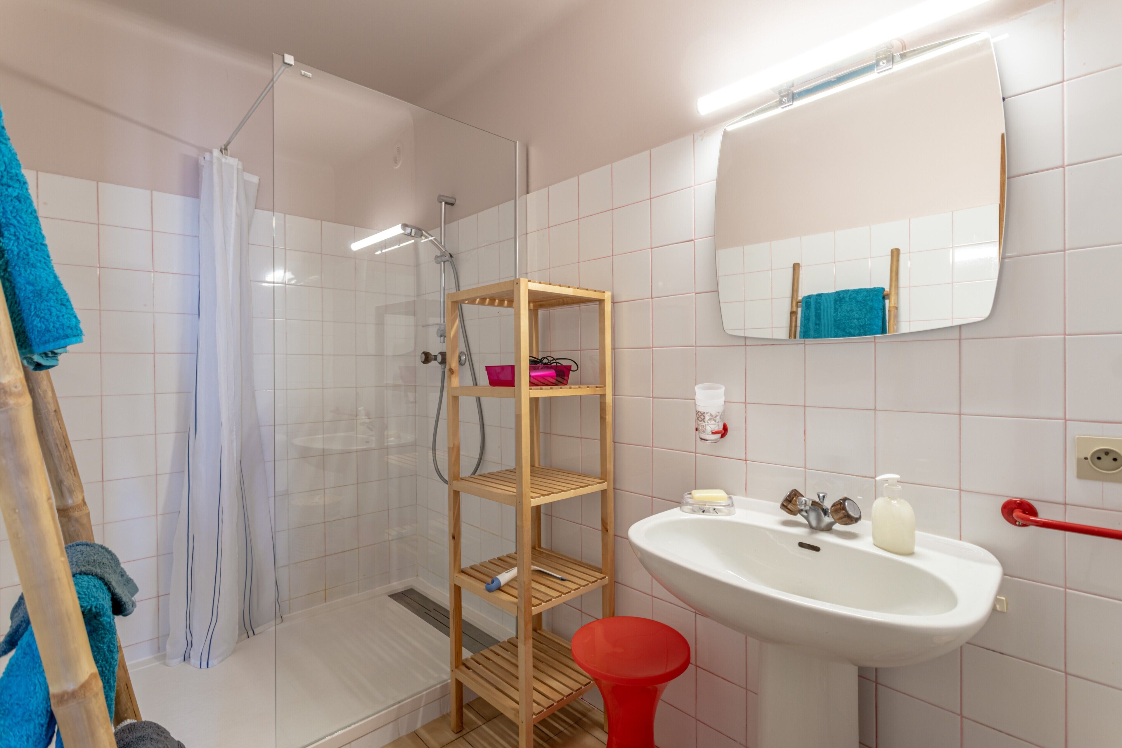 Une salle de bain avec une douche, une étagère en bois, un lavabo et un miroir.