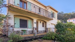 A two-story house with a balcony, a stone facade, and a garden area with gravel and plants.