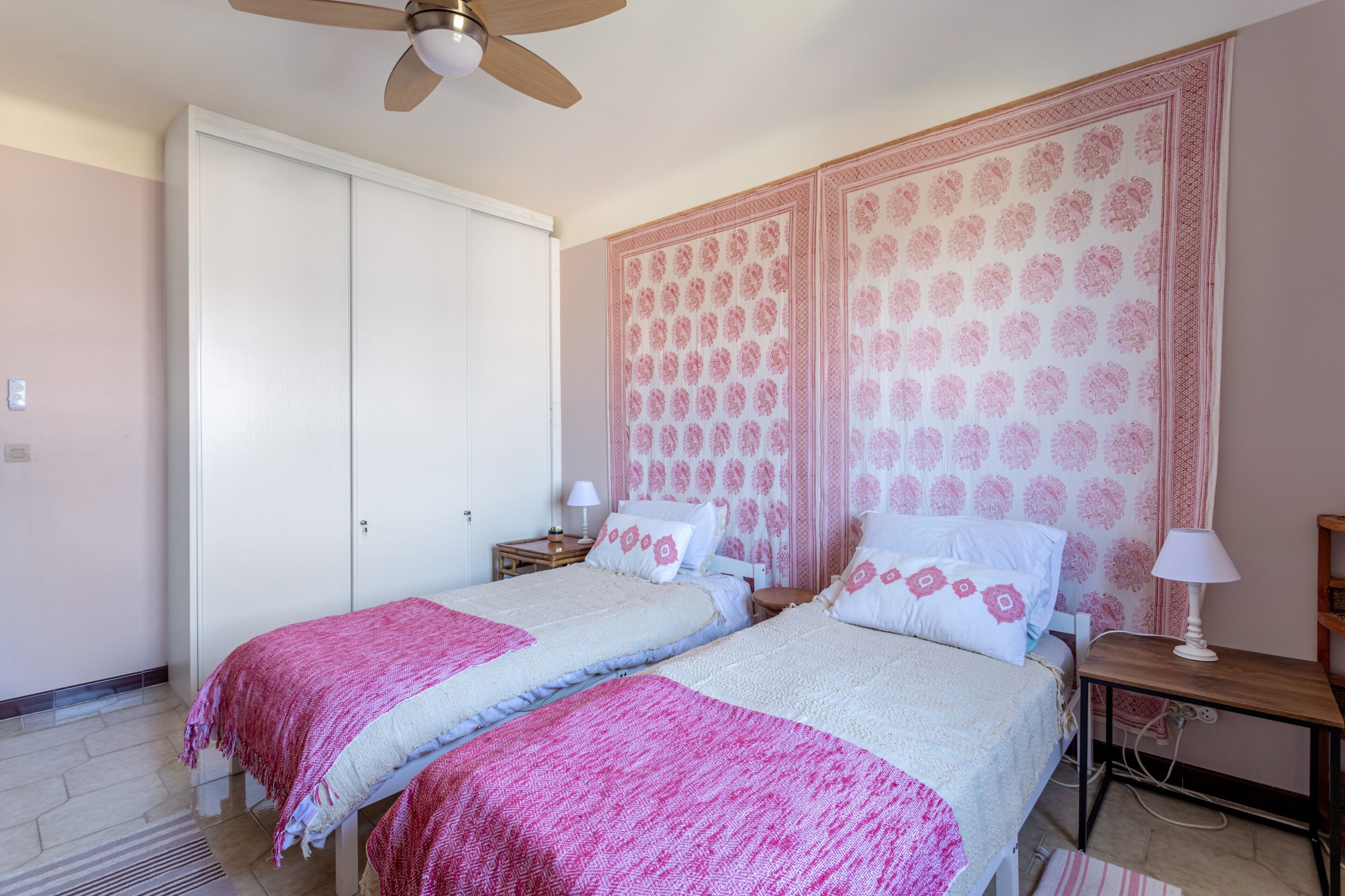 Un dormitorio con dos camas, ventilador de techo, armario y cabecero decorativo.